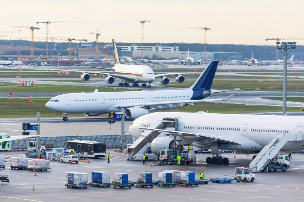 Plusieurs avions sur un tarmac d'aéroport très fréquenté avec du personnel au sol chargeant des bagages et des bagages.