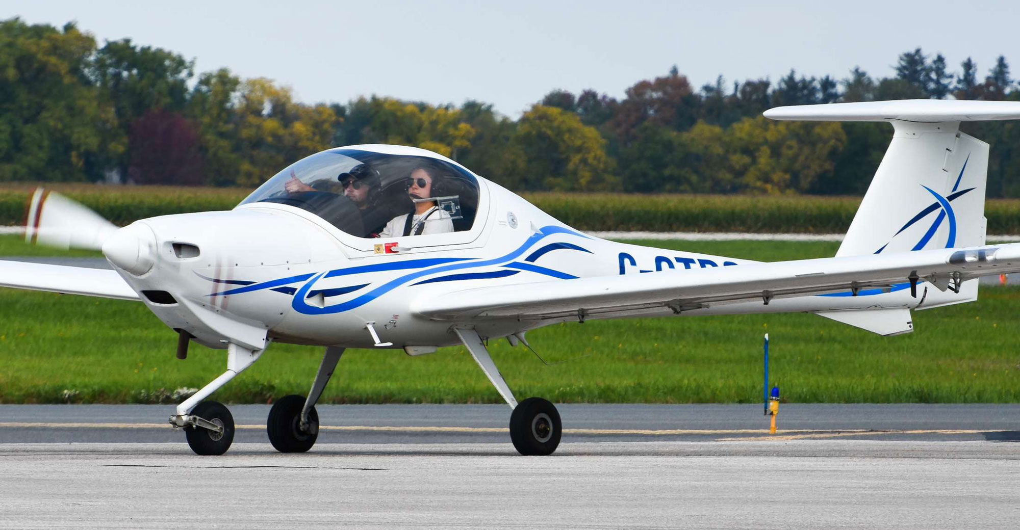 Small white training aircraft taxiing on a runway with a student pilot and instructor seated in the cockpit
